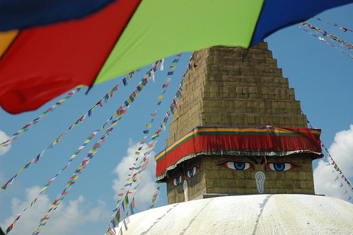 Sunny day with puffy clouds as the eyes oversee new prayer flags beings raised. Shot from a restaurant across from the Bodha Stupa, under an umbrella, Kathmandu, Nepal by Wonderlane