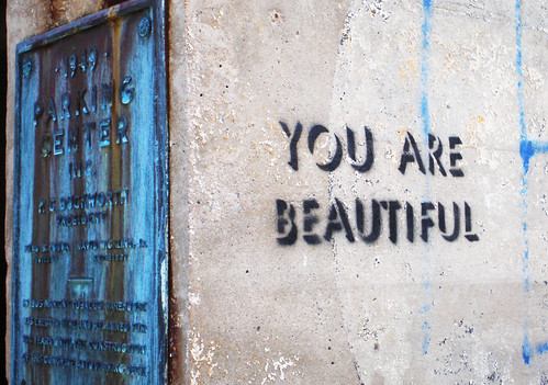 Image Description: a wall with a bright blue door. On the side of the wall is graffittied in stencil "You are Beautiful."