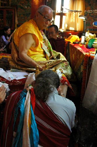 Tashi Paljor, a student from Seattle, Washington, wearing a red and white adi, makes the offering of the mandala of the universe with 5 colored katags to His Holiness Jigdal Dagchen Sakya, Tharlam Monastery of Tibetan Buddhism, Boudha, Kathmandu, Nepal by Wonderlane