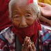 Elder Tibetan woman praying wearing face mask to protect against the dust, during Lam dre, Tharlam Monastery, Boudha, Kathmandu, Nepal