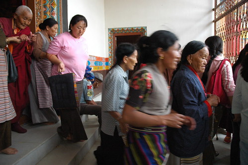 Tibetan woman leaving, wearing traditional chubas, an elderly nun is helped down the stairs, one woman carrying her seat, Sakya Lamdre, porch, Tharlam Monastery of Tibetan Buddhism, Boudha, Kathmandu, Nepal by Wonderlane
