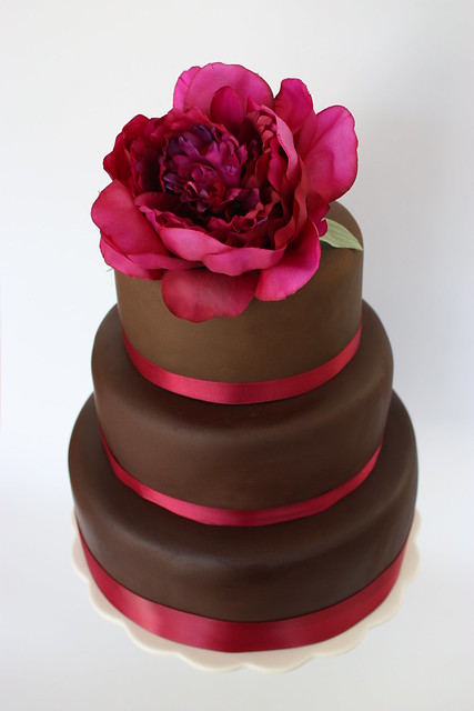 A 3 tier chocolate fondant covered cake decorated with dark pink ribbon and