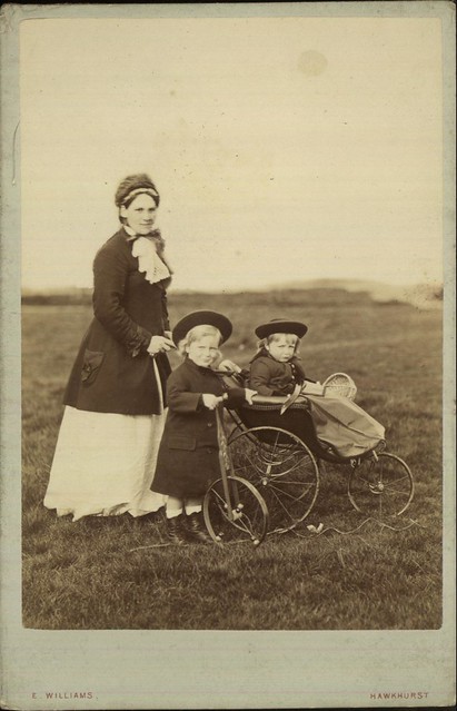 Outdoor portrait of a mother, or nurse, pushing a baby in a pram and with a young child with a bicycle by E Williams of Kent, 1890-1900.