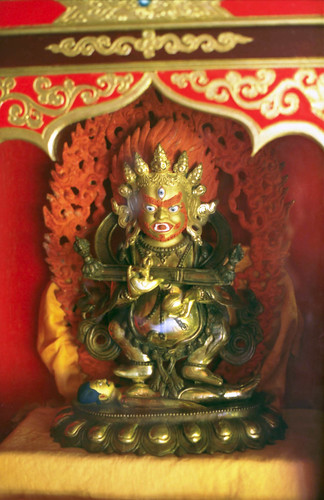 Statue of Shri Mahakala, protector, orange hair, crown of skulls, holding chopper and skull, ritual stick, burning flames of wisdom, Tibetan Buddhism, Sakya school monastery, Pharping, Nepal in 1990 by Wonderlane