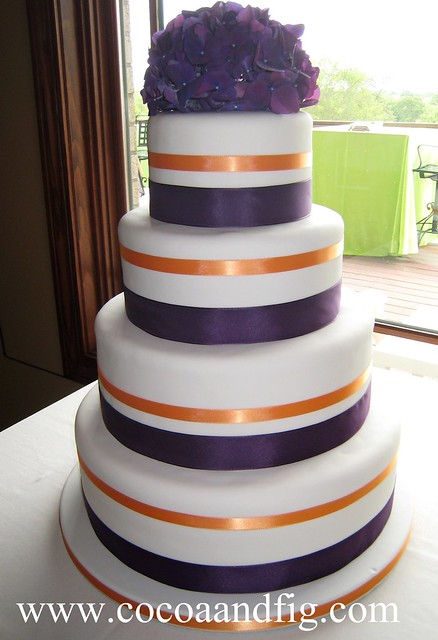 Covered in fondant and decorated with deep purple and orange ribbon