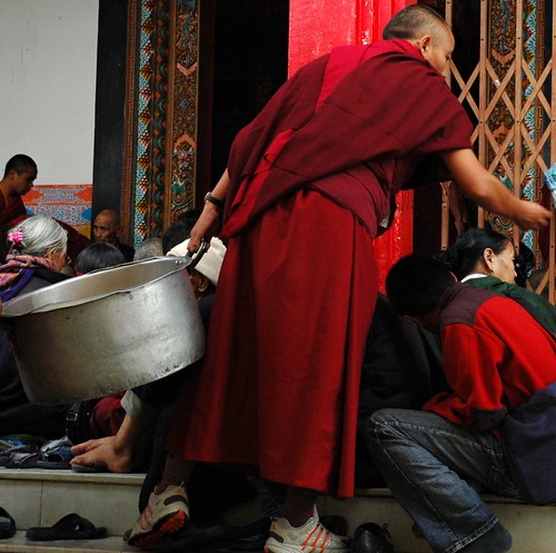 Old Monk in sneakers holding a large pot distributing dharma muffins to monks and nuns, Lamdre, Tharlam Monastery, Boudha, Kathmandu, Nepal by Wonderlane