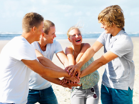 Happy team of young teens with their hands together at the beach