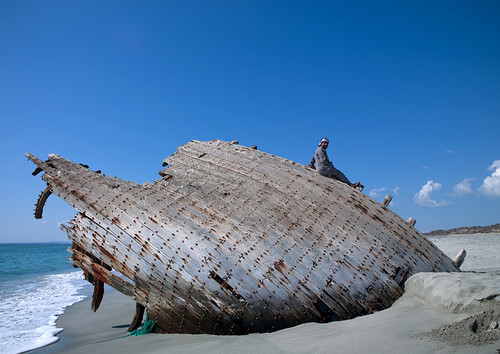 Man on a dhow wreck on the beach, Masirah Island, Oman by Eric Lafforgue