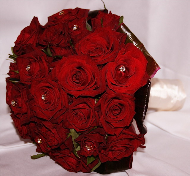 Compact hand tied bridal bouquet of open red roses and detail of diamante