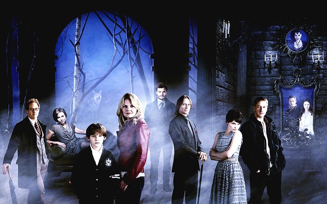 The all-white cast of Once Upon a Time stands in a shadowy forest. 