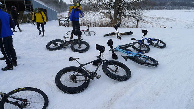 Surly fat bikes laying in a snowy area with cyclists standing around them