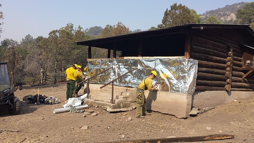 Forest Service firefighters wrap a cabin in Aluminized Structure Wrap to protect the building from radiant heat and burning embers from the Silver Fire on the Gila National Forest in 2012. Wrapping a structure is the best protection strategy when it's too dangerous to stay. (US Forest Service photo)