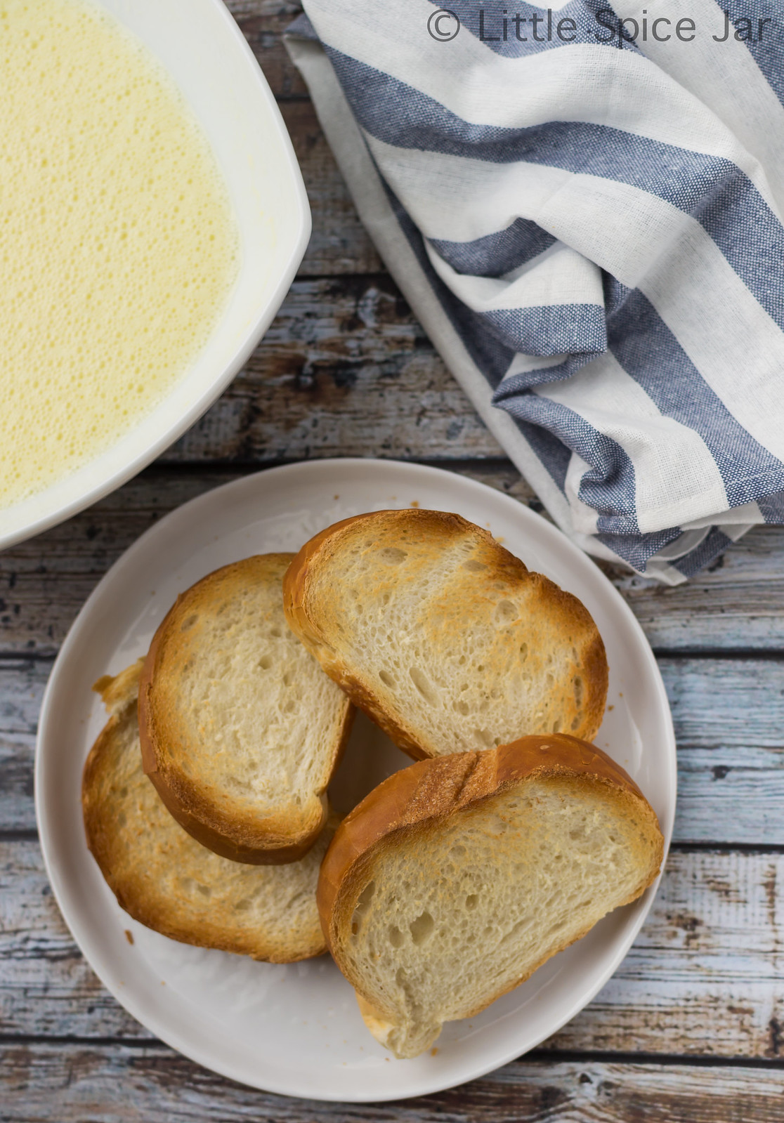 toast bread on white plate with custard in large bowl with striped towel on faux wood surface