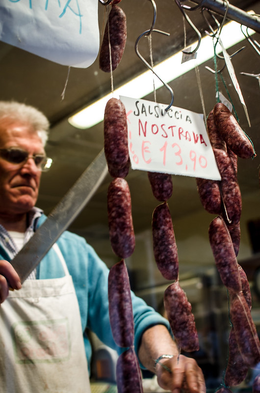 A Venetian butcher prepares some sausage for a customer.