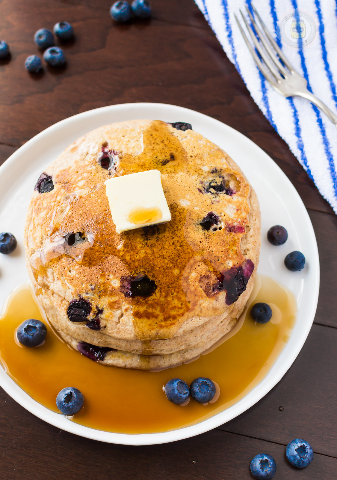 stack of blueberry pancakes with butter sitting in a puddle of pancake syrup
