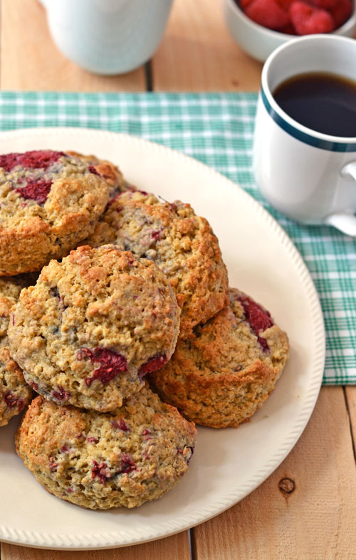 Raspberry scones piled on a white plate next to a mug of coffee
