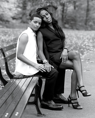 a trans woman poses on the lap of a trans man in a park