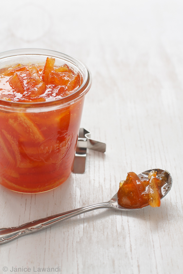 A spoonful of marmalade next to a big jar homemade orange, grapefruit and lemon marmalade featuring long, thick strips of citrus peel.