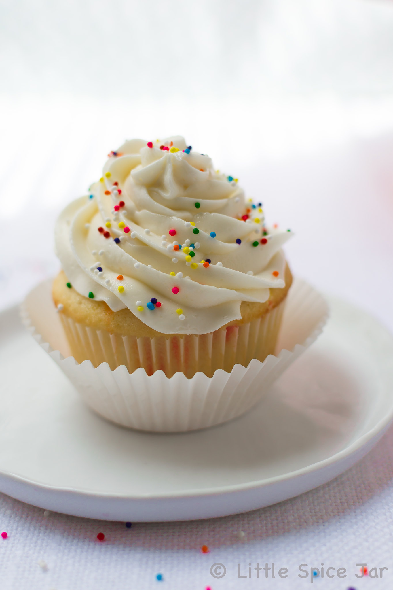 prepared funfetti cupcake with whipped topping and sprinkles on white plate on white surface