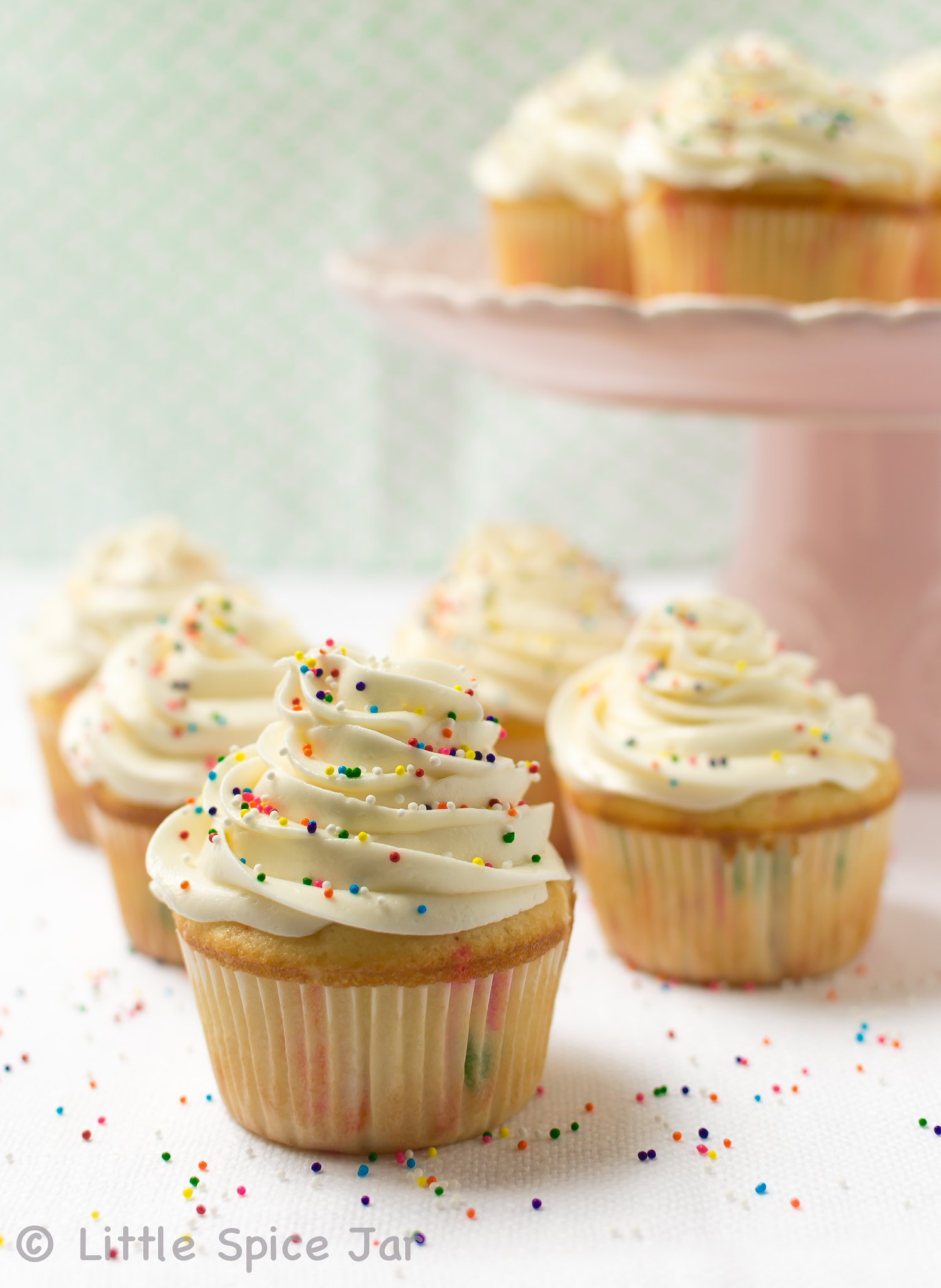 prepared funfetti cupcakes on white linen with cake stand holding more cupcakes in the back