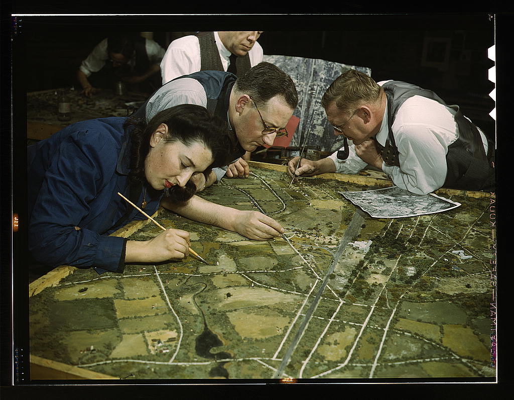 Vintage photograph of a camouflage class in New York. Image depicts a group of people adding final details to a map. Image without historical context implies they are making the map themselves.