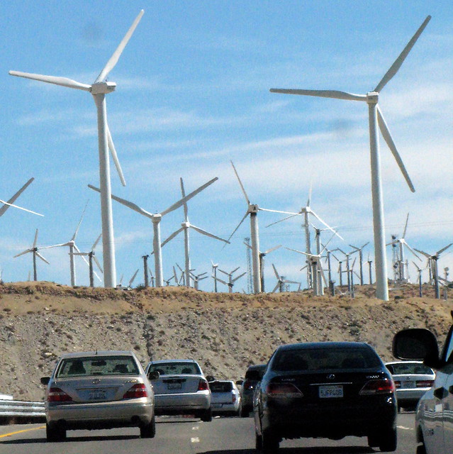 A road full of cars driving toward a windmill farm