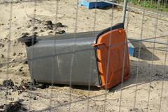 Omgevallen vuilnisbak achter een hek op een bouwterrein.