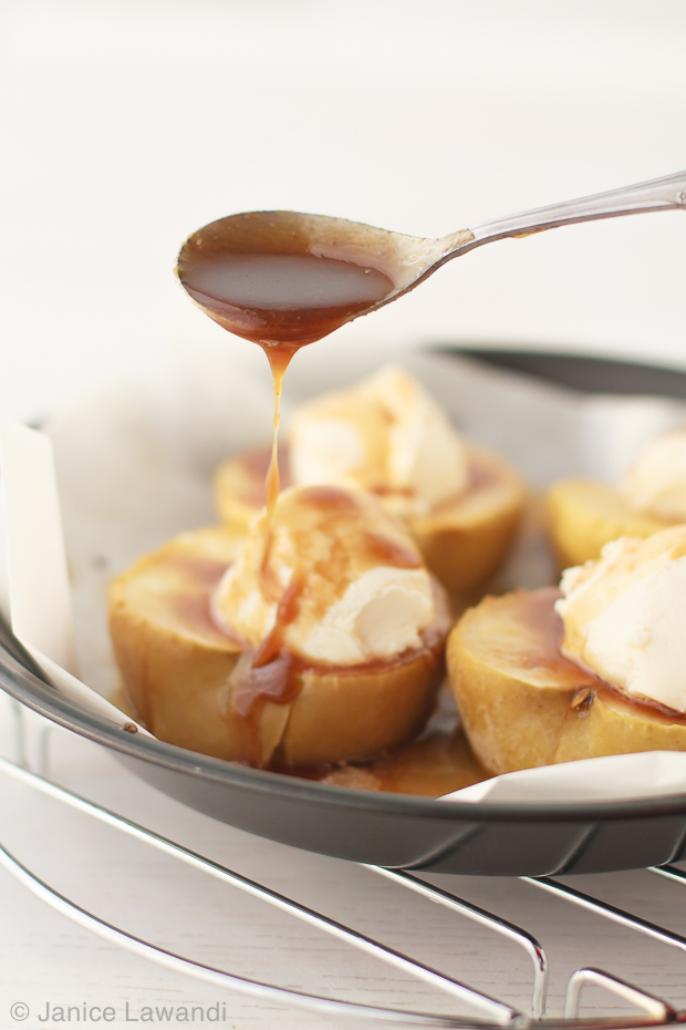 Baked apples with ice cream and brown butter whiskey sauce drizzled on top with a spoon.