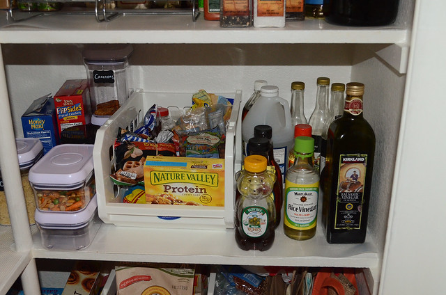 Plastic containers filled with food and bottles of vinegar in a pantry.