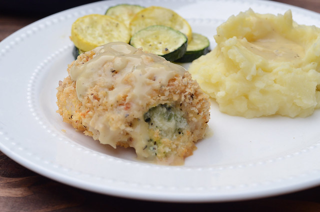 A serving of Broccoli Cheese Stuffed Chicken on a white plate with mashed potatoes and zucchini.