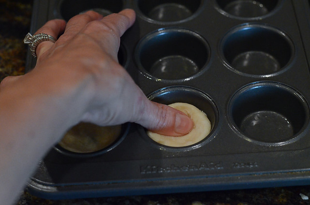 A thumb presses into dough in a mini muffin pan.