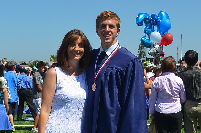 Boy #4 in his graduation outfit standing with Valerie.