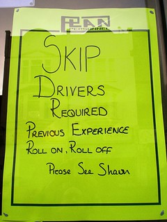 A neon-yellow poster with a printed “Plan Personnel” header and writing in black pen: “Skip Drivers Required. Previous experience. Roll on, roll off. Please see Shaun [or possibly Sharon].”