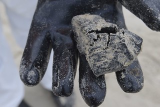 A crew member displays a clump of tar recovered during clean-up operations at the beaches of National Seashore Park April 2, 2014. Local, state and federal agencies are working together to remove any materials containing oil that may have washed up ashore. (U.S. Coast Guard photo by Petty Officer 3rd Class Carlos Vega)