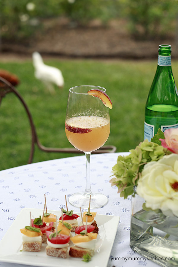 A beautiful peach bellini with prosecco sits on an outdoor table with summer appetizers. 