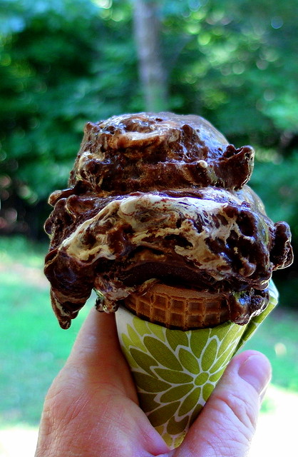 A hand holding a waffle cone filled with Triple Chocolate Coffee Peanut Crunch Gelato.