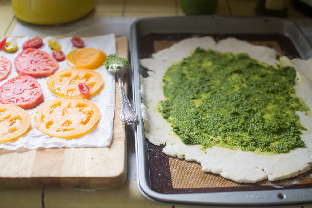 Once dough is rolled out, transfer it to a non-stick baking sheet. The dough is fragile so it needs to be on the baking sheet before toppings are added. Spread a thin layer of pesto onto the dough leaving a 1 inch border around.