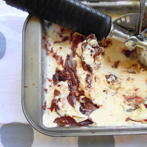 Overhead shot of metal container of vanilla malt ice cream with fudge sauce and an ice cream scoop.