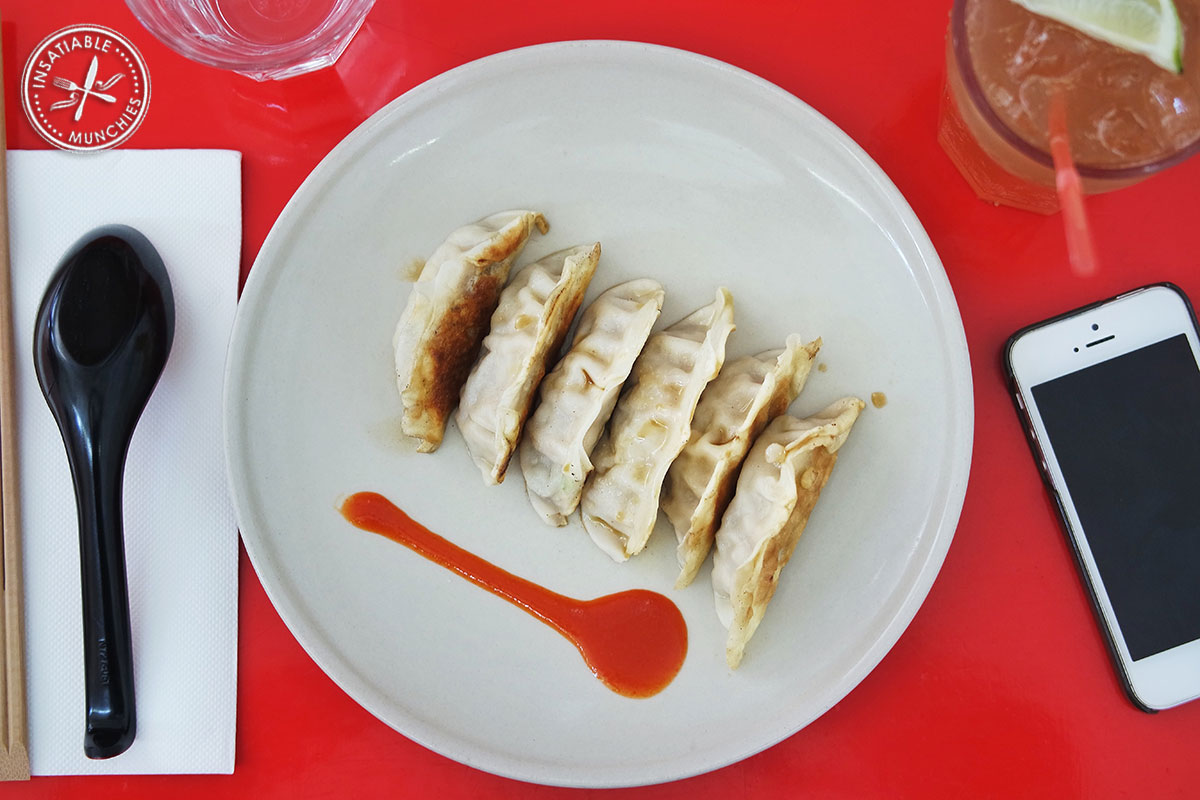 Gyozas served on a round plate with a line of sriracha